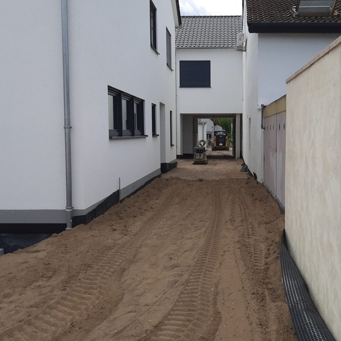 Zufahrt mit Durchfahrt und Rüttler bei vorbereiteten Maßnahmen für Pflasterarbeiten